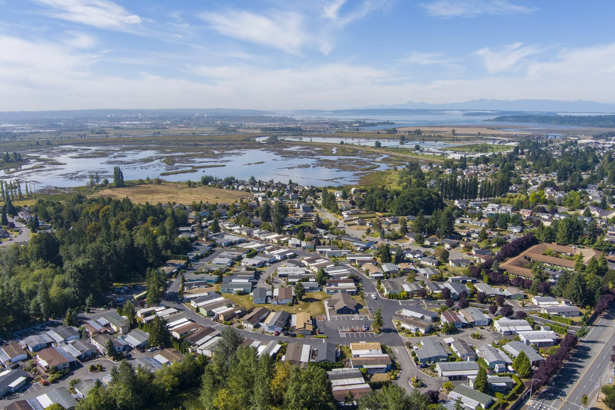 Aerial view of a manufactured home community in Marysville, surrounded by tall trees and a lake in the background.